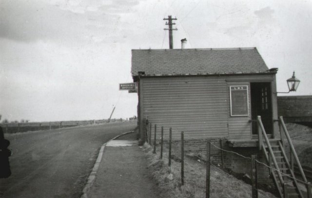 A wooden railway station building to the right with the road on the left