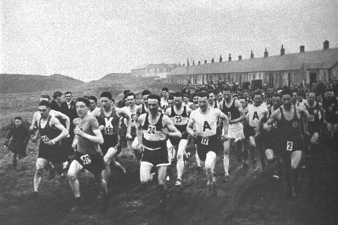 large group of runners in a competition through the mining village of Benquhat. The houses are in the background 