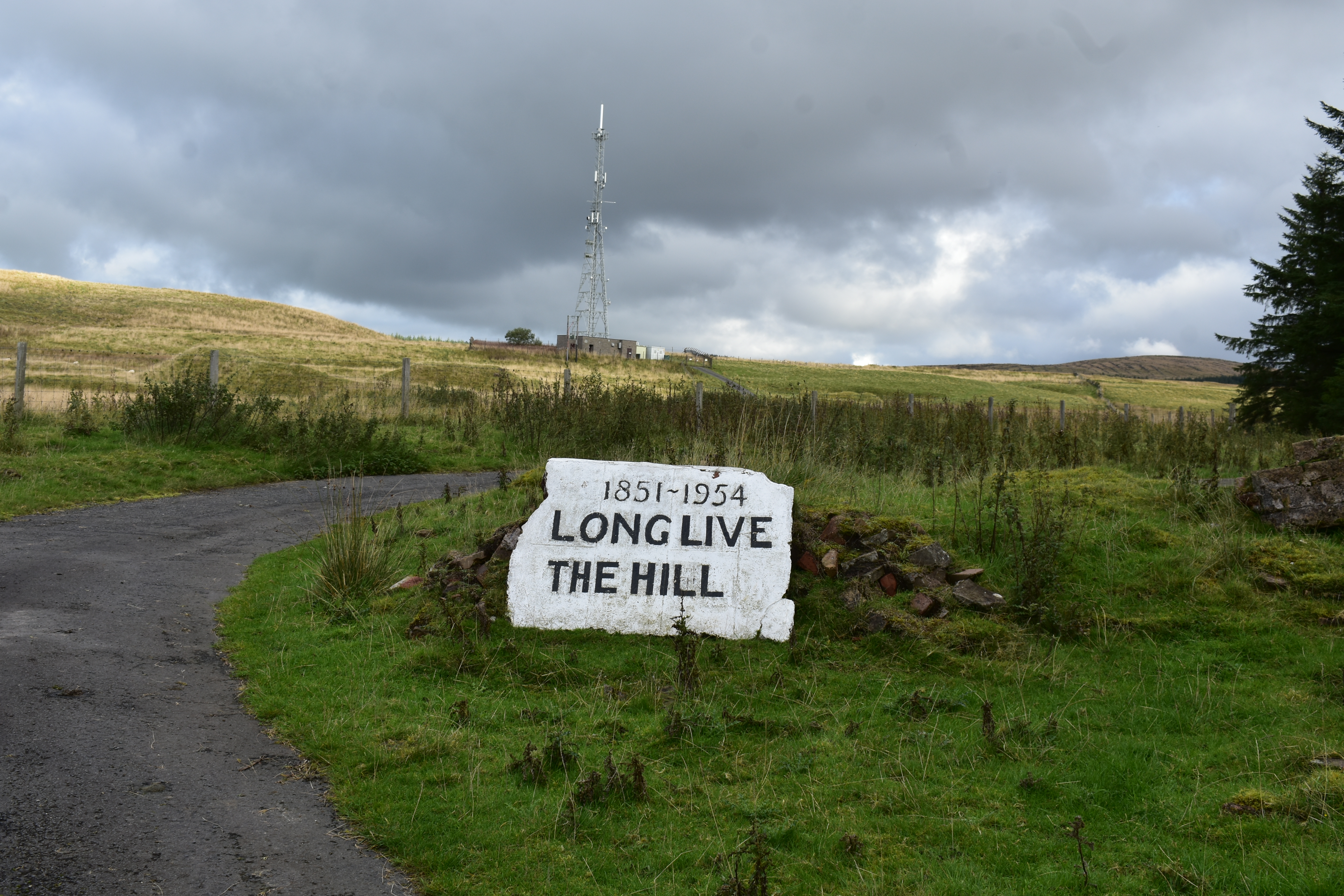 White painted marker saying Long Live the Hill next to a pathway surrounded by grass and hills.