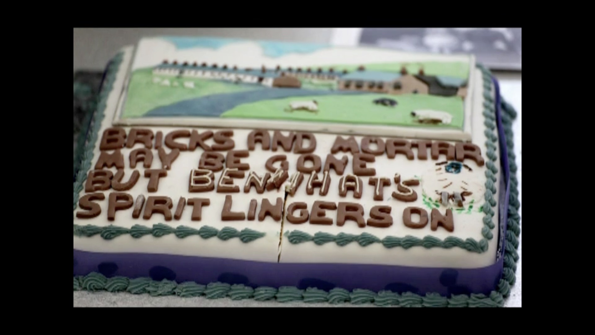 photo of a cake with a scene on it of grass hills, a row of houses and sheet. The message reads: Bricks and mortar may be gone but Benwhat's spirit lingers on.