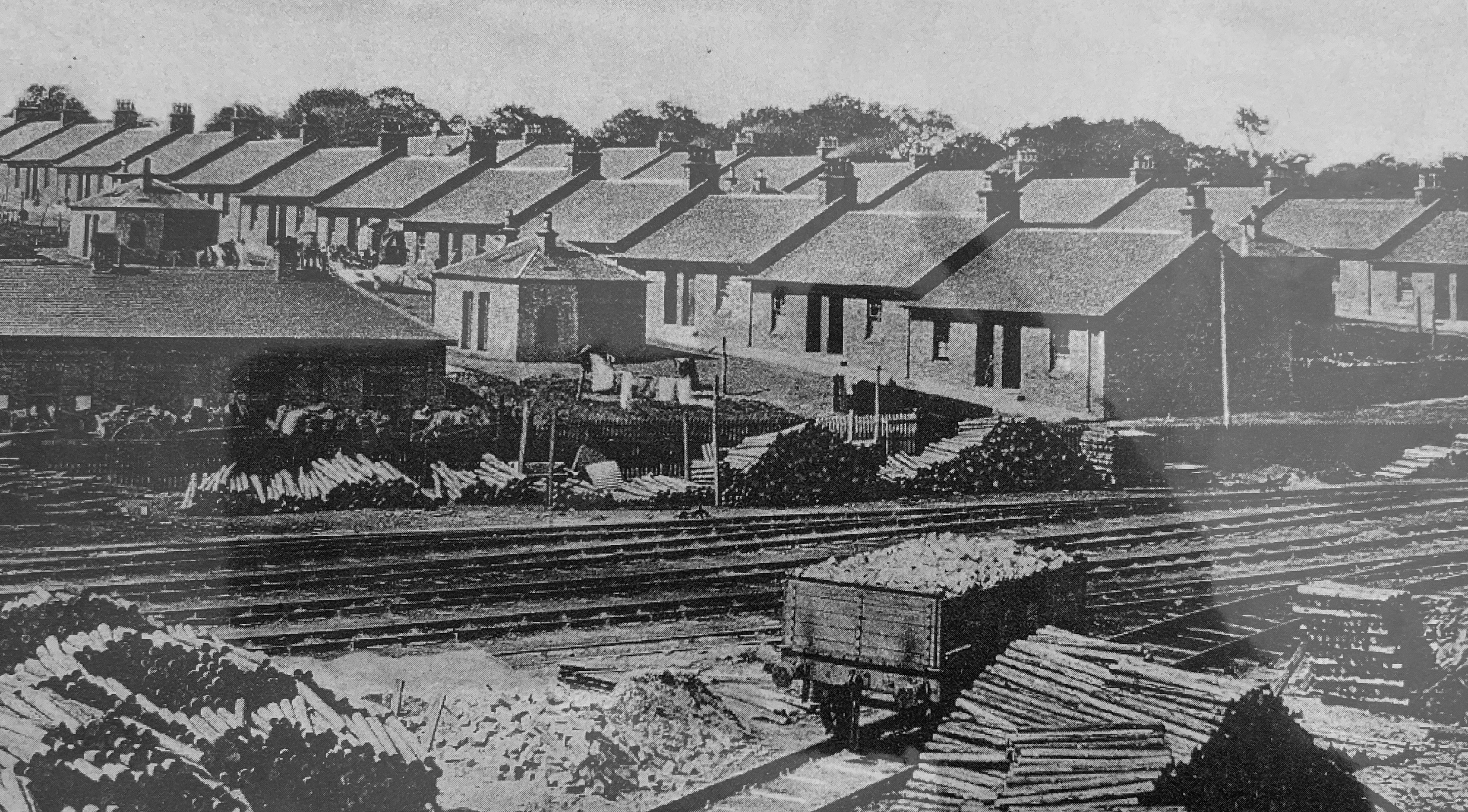 black and white photograph of two row of single storey brick houses with railways tracks in the foreground