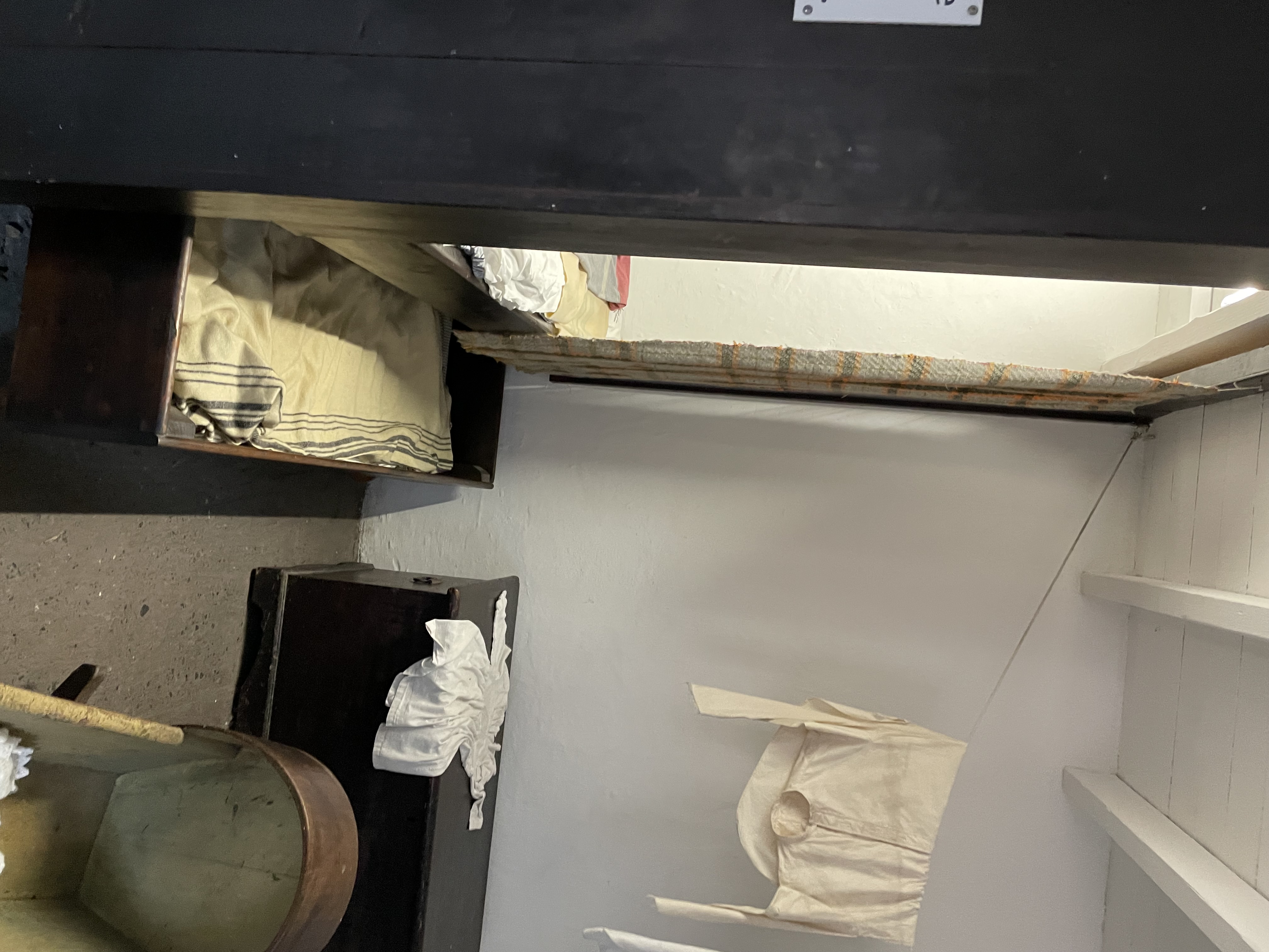 Photograph of a room showing a bed with a pull out bed underneath, some dark wooden furniture in on teh far war and some white shirts hanging to dry