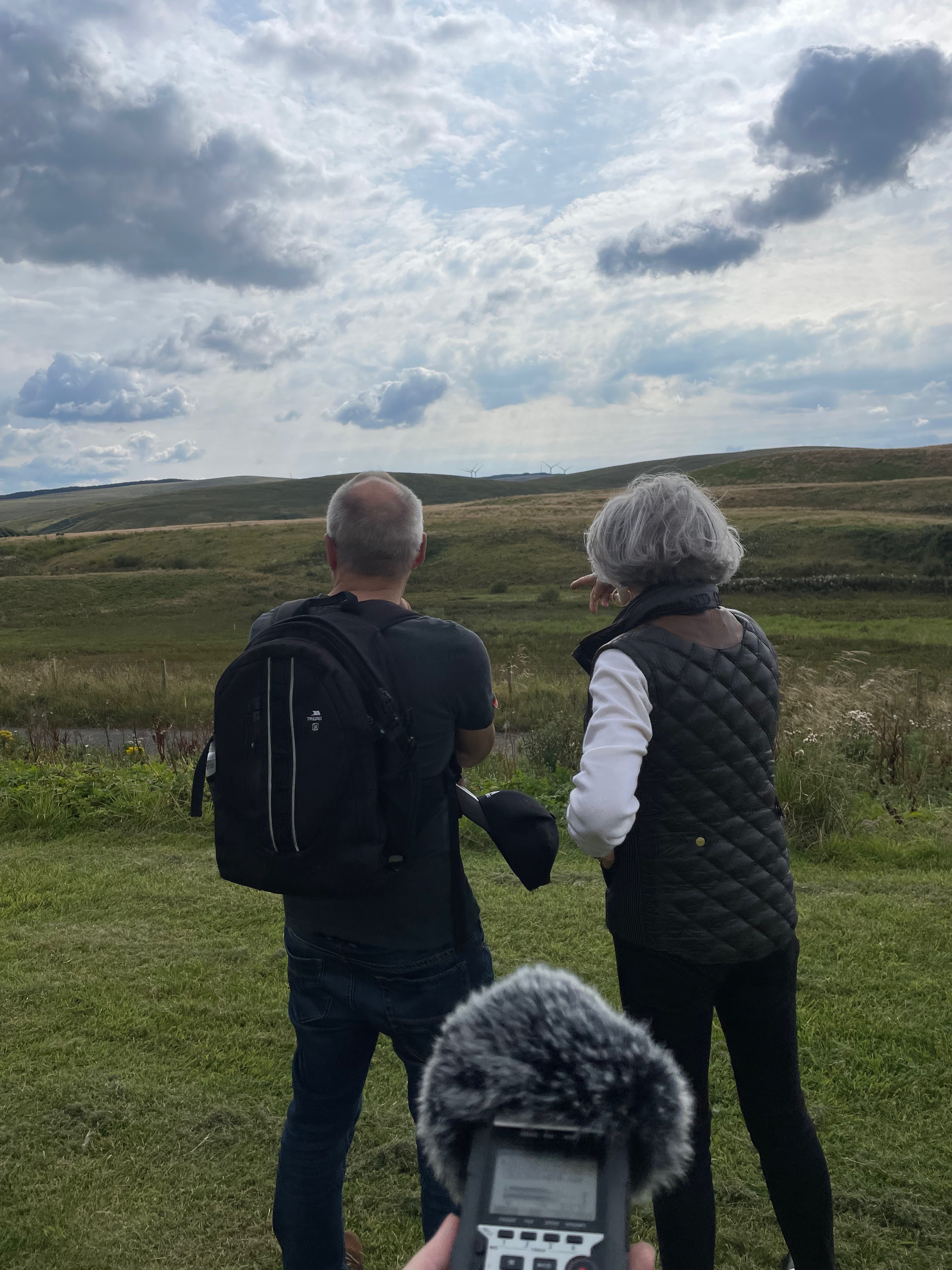 Two figure, one male and one female, looking at a field with hills in the background. A recorder is the in the foreground