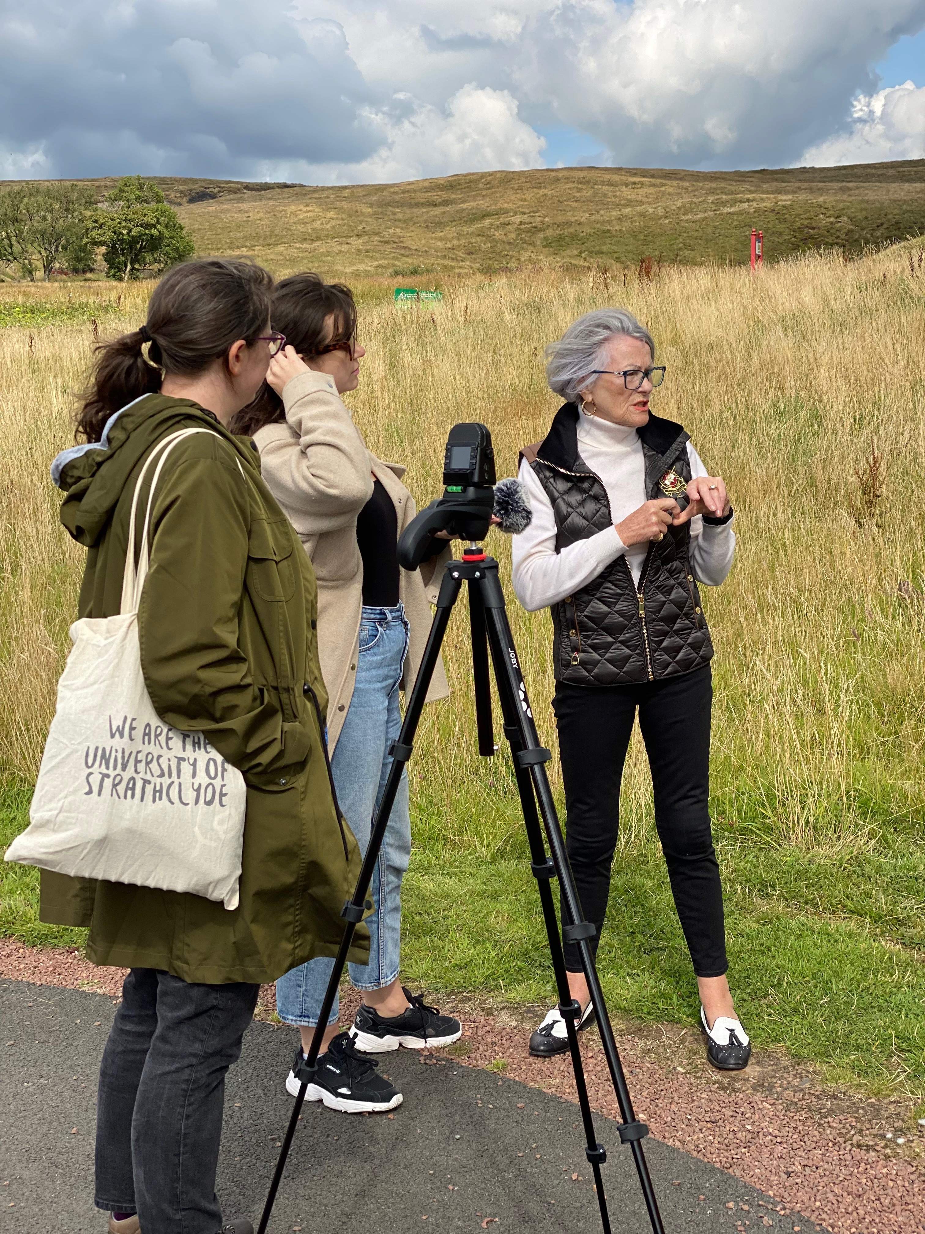 Three women standing in a rural area next to a video camera.