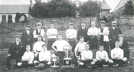 Photograph in black and white of a football team from the 1930s with two trophies